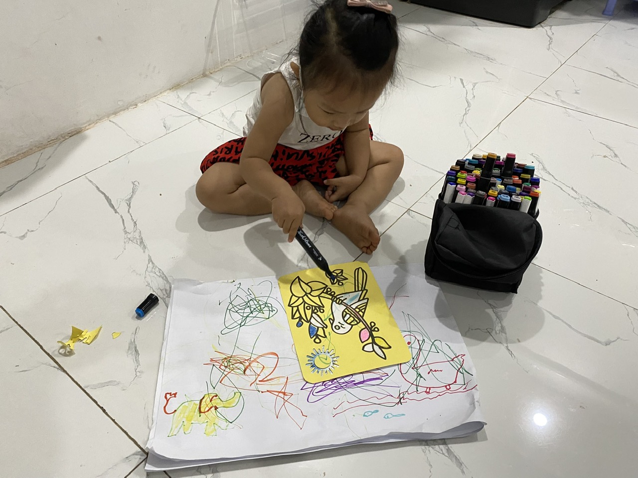Bé Gia Nguyên hai tuổi ngồi bệt dưới sàn, tự vẽ tô kín tờ giấy